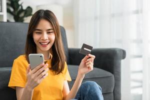 feliz joven mujer asiática con tarjeta de crédito y usando un teléfono inteligente para comprar en línea con pago en banca por Internet. foto
