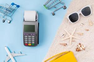 vista superior de tarjetas de crédito y máquina lectora de tarjetas con factura y estrellas de mar, gafas de sol en la arena. foto