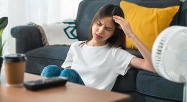 joven asiática cansada sentada en el sofá y con dolor de cabeza por migraña. foto
