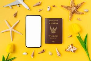 concepto de horario de verano, pantalla de maqueta de teléfono inteligente con pasaporte y accesorios de playa en el fondo amarillo. foto