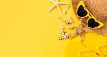 concepto de horario de verano, vista superior con espacio de copia de gafas de sol y sombrero con estrellas de mar, chanclas sobre fondo amarillo. foto