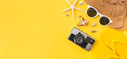 Summer time and travel concept, top view of camera and flip flops, sunglasses on hat with starfish on yellow background. photo