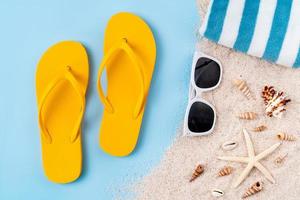 Top view with copy space of yellow sandals with starfish and shells, sand on blue background. photo