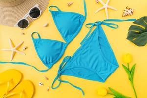 vista superior de bikini y gafas de sol con accesorios de playa en el fondo amarillo. concepto de horario de verano. foto