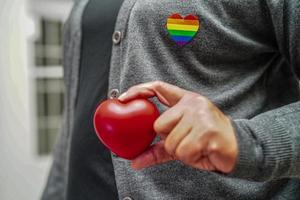 Asian woman holding red hert with rainbow flag, LGBT symbol rights and gender equality, LGBT Pride Month in June, LGBTQ, LGBTI, LGBTQA, LGBTQIA photo