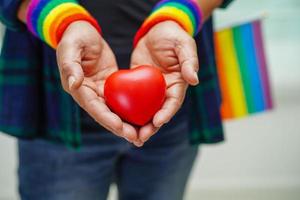 Asian woman holding red hert with rainbow flag, LGBT symbol rights and gender equality, LGBT Pride Month in June, LGBTQ, LGBTI, LGBTQA, LGBTQIA photo