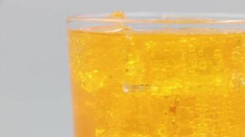 orangefarbenes Sprudelwasser mit Eis im Glas. Rotieren Sie ein Glas Orangen-Mineralwasser-Getränk auf weißem Hintergrund. video