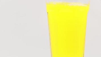 Pour orange juice into a rotating glass on a white background. video