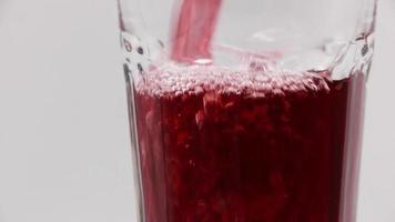 Pour pomegranate juice into a rotating glass on a white background. video