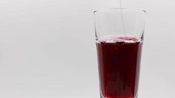 Pour pomegranate juice into a rotating glass on a white background. video
