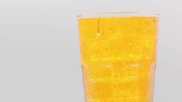 Orange sparkling water with Ice in glass over white background. video