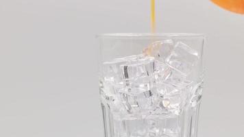 Pouring Orange sparkling water with ice cubes close-up. Orange sparkling water with Ice in glass. Rotate glass of Orange sparkling water drink over white background. video