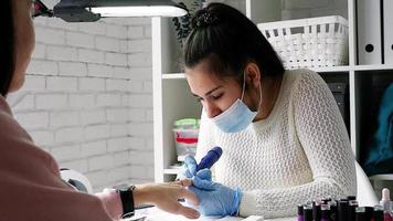 weibliche maniküristin in einer gesichtsmaske, die eine maniküre im salon macht. meisterin bedient ihren kunden. Nagelpflegeverfahren. video