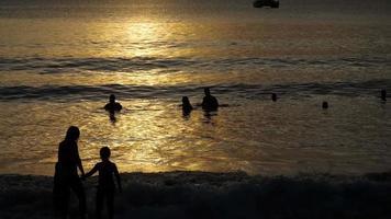 hermosa puesta de sol con siluetas de personas que disfrutan del océano. video