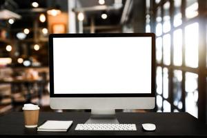 monitor de computadora, teclado, teléfono inteligente de taza de café, tableta y mouse con pantalla en blanco o en blanco aislado está en la mesa de trabajo en la cafetería foto