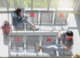 Blur top view background of young Asian travelers sitting on public waiting seat with social distancing symbol to avoid COVID-19 infection. light effect. photo