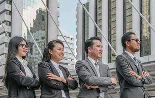 equipo profesional de negocios asiáticos de pie con los brazos cruzados con confianza sonriendo en el fondo de la ciudad. foto