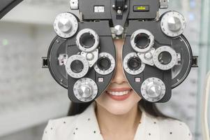 una joven clienta que está siendo examinada con una prueba visual usando un dispositivo de medición de la vista de optometría bifocal por un oftalmólogo en el centro óptico, concepto de cuidado de los ojos. foto