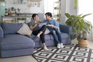 joven pareja gay sonriente con comida saludable en la sala de estar en casa, lgbtq y concepto de diversidad. foto