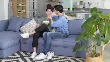 Young smiling gay couple having popcorn while watching TV in the living room at home, LGBTQ and diversity concept. photo