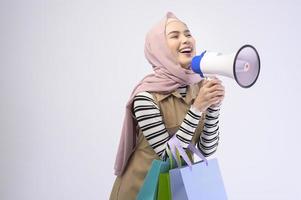 Young beautiful muslim woman in suit holding colorful shopping bags over white background studio photo