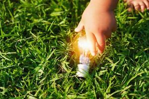 children hand holding lightbulb on green grass. concept eco energy photo