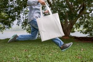 mujer joven sosteniendo una bolsa de algodón y saltando en el fondo de la hoja verde foto