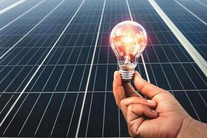 hand holding light bulb with solar panel background photo