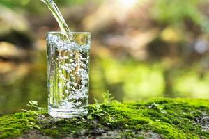 vierta agua en un vaso sobre hierba verde en la naturaleza foto