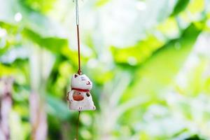 maneki neko es una muñeca de gato de la suerte japonesa que cuelga en la ventana con un fondo de naturaleza verde foto