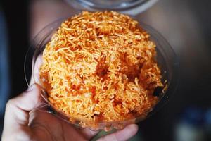 Hand holding Sweet and Sour crispy rice noodle vermicelli in clear plastic box photo
