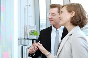 Successful businessman and businesswoman writing good ideas on sticky notes pasted on glass wall in modern office meeting. photo