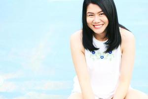 Beautiful asian woman in white dress smiling on blue concrete floor. Thai girl enjoy on holiday concept. photo