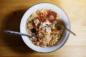 Tradition Thai food Hot and spicy Seafood instant noodle in white bowl with fork and spoon on wooden floor background photo