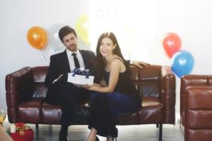 dulce pareja amor feliz con caja de regalo sorpresa novia en fiesta de navidad, celebración de cumpleaños víspera de año nuevo, decoración de día de san valentín con globo colorido en sofá marrón en sala de estar foto