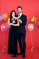 dulce pareja amor sonrisa y pasar romántico bebiendo vino en navidad y celebrando la víspera de año nuevo, día de san valentín con globo colorido sobre fondo rojo foto