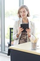 Businesswoman in white suit hand holding tablet for searching on website and thinking in job at workspace in office photo