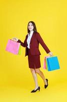 Beautiful woman in red suit smile and hand holding colorful shopping paper bags isolated on yellow background. photo