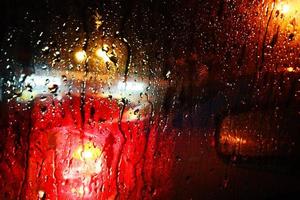 textura de gotas de lluvia en el cristal de la ventana con luz de la calle paisaje urbano borroso abstracto. enfoque suave foto
