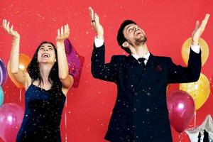 la pareja ama la sonrisa romántica y el baile en la fiesta de Navidad, la hora del cumpleaños y la celebración de la víspera de año nuevo y la decoración con globos coloridos y brillo dorado sobre fondo rojo foto