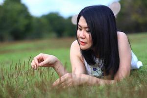 Beautiful asian woman in white dress relax and smiling on green field in natural park. Young Thai girl enjoy on holiday with sunlight in garden photo