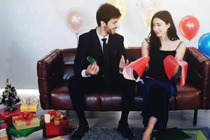 dulce pareja ama sonreír y pasar un tiempo romántico de navidad y celebrar la víspera de año nuevo en la decoración de un sofá marrón con árbol de navidad, globos coloridos y cajas de regalo en la sala de estar en casa foto