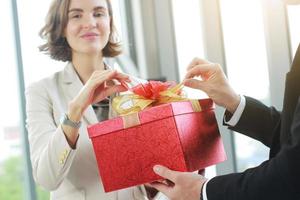 el empresario sorprende y le da una caja de regalo roja a la empresaria en el cargo por cumpleaños. navidad, feliz año nuevo y san valentín, concepto de día. cerrado en el cuadro de regalo rojo. foto