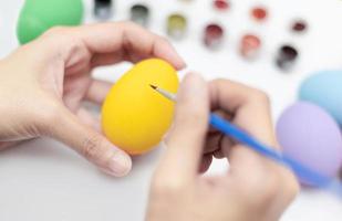 Female hands holding a paintbrush to paint the yellow eggs. Handicraft concept. Happy Easter day. Decorative concept. photo
