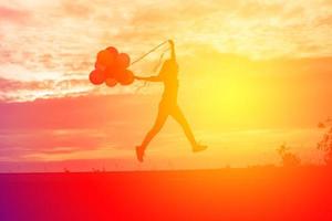 silhouette of young woman holding colorful of balloons with sunset photo