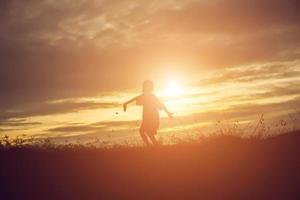 silueta de niño, momentos de alegría del niño. en la puesta de sol de la naturaleza foto