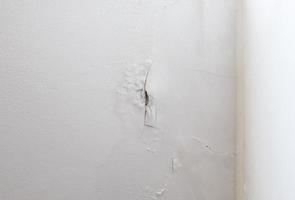 la pared de pintura blanca se está pelando y hay una grieta larga cerca de la esquina del dormitorio. foto