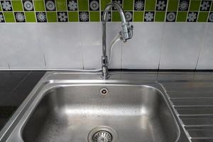 The clean metal sink with the chrome tap after washing on the modern counter. photo