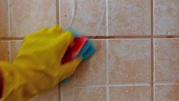 Hand in yellow protective glove washes tile with foam on ceramic tile background.Home cleaning. video