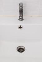 The ceramic sink basin with the dirty faucet near the white wall of the restroom. photo